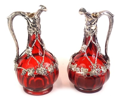 A pair of late 19th/early 20thC ruby tinted glass claret jugs, each with silver plated mounts, cast with grapes, vines, branches, etc., 36cm high including stoppers, in a fitted box.