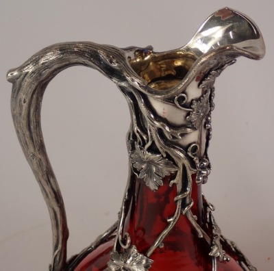 A pair of late 19th/early 20thC ruby tinted glass claret jugs, each with silver plated mounts, cast with grapes, vines, branches, etc., 36cm high including stoppers, in a fitted box. - 2