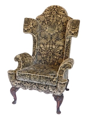 An unusual wingback armchair in mid 18thC style, upholstered in gold and black fabric, decorated with leaves, grapes, etc., on four carved cabriole legs and pad feet.