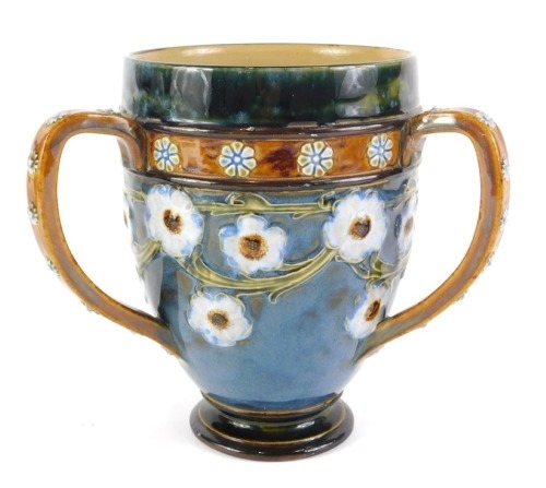 A Royal Doulton stoneware tyg, with sgraffito and tube lined decoration of a band of flowers and leaves, the handles applied with roundels, indistinct decorators mark and impressed mark numbered 5011, 18cm high.