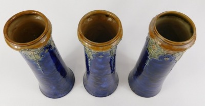 Three Royal Doulton stoneware vases, each decorated with flowers, stylised leaves in Art Nouveau style, in green, on a mottled blue ground, impressed marks to underside, indistinct makers monograms, each 32cm high. - 2