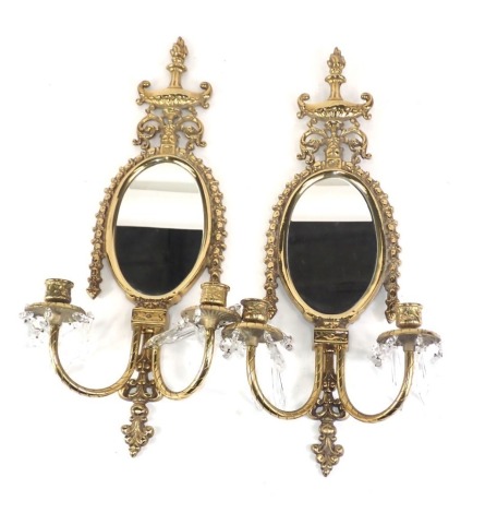 A pair of gilt brass oval wall mirrors, with oval mirror plate and two candlesticks with crystal droplets.