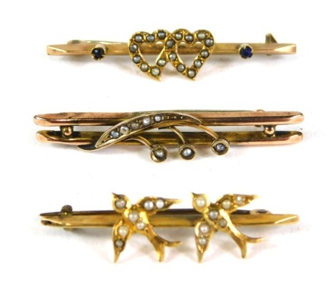 Three bar brooches, comprising a spray fern, yellow metal stamped 9ct, 4cm wide, a 9ct gold swallow and seed pearl brooch, 3.5cm wide, a 9ct gold love heart seed pearl and sapphire bar brooch, 4cm wide, 5.2g all in. (3)