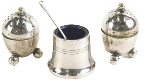 A silver plated three piece cruet set, comprising two pepper pots, on bun feet, 6cm high, and a plated mustard with blue glass liner and later spoon, 4cm high.