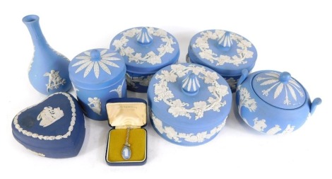 A collection of Wedgwood blue Jasperware, comprising two collectors jars and covers, miniature urn and cover, miniature biscuit barrel, bud vase, dark blue Jasperware heart trinket, and a necklace.