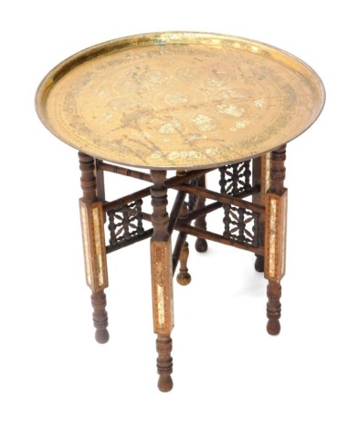 An Eastern brass tray table, the circular tray with hammered decoration, on a hardwood base with mother of pearl and boxwood inlay, 50cm high, 57cm diameter.