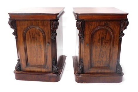 A pair of Victorian mahogany cabinets, each with a square top with rounded corners, with applied scroll caryatids and single door, each with separate linings, one with two drawers, and another with cupboard door and shelf, 84cm high, 55cm wide, 60cm deep.