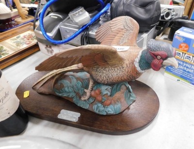 A pottery model of a pheasant in flight, on wooden plinth.