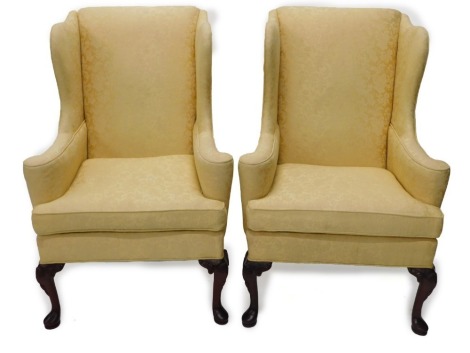 A pair of mahogany wingback armchairs in George I style, each upholstered in gold damask fabric, on cabriole legs headed by shells and with leaf carved brackets and pad feet.