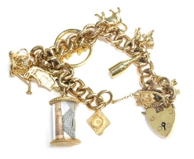 A 9ct gold charm bracelet, with curved link chain, a heart shaped padlock with safety chain, and various 9ct gold attached links to include owl on perch, elephant, bottle, cat, kettle, love heart padlock, roll of money, graduation cap, etc., 64.2g, all in