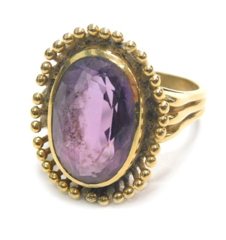 An 18ct gold amethyst dress ring, the chunky oval amethyst, with petalated floral border, on three strand shoulders, ring size M½, 8.8g all in.