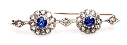 An Edwardian sapphire and diamond bar brooch, set with two rose cut sapphires, in a circular surround of diamonds, interspersed with diamonds in a lozenge setting, in white metal, 6.2g all in.