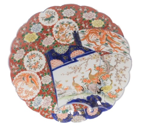 A Meiji period Japanese Imari charger, with scalloped border and hand painted decorative scroll panel of cranes and ducks, and further vignettes of flowering foliage, phoenix and chrysanthemums, on an iron red ground, 40cm diameter.