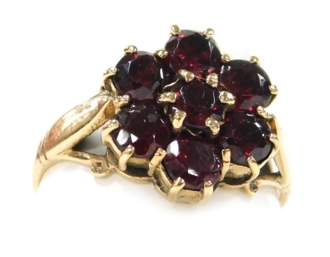 A garnet seven stone flower head ring, in a yellow metal mount, hallmarks worn, size M, 2.9g.