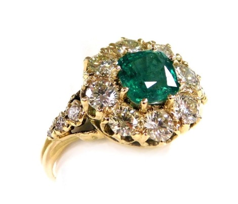 An emerald and diamond ring, the cushion shaped emerald in a surround of eight brilliant cut diamonds with graduated diamond set shoulders, in a yellow metal basket mount, emerald approximately 1.2ct, diamonds approximately 1.45ct, size 0, 4.8g all in.