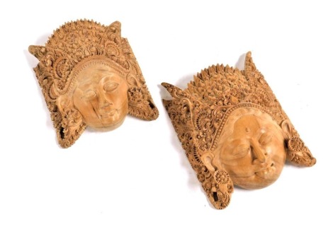 A pair of Balinese carved wooden Hindu figural masks, with ornate head dresses, 21.5cm and 18.5cm high.