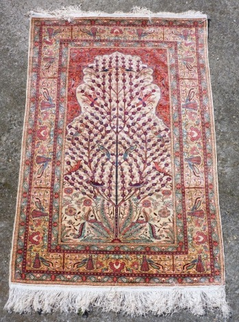 A Persian Kayseri silk Tree Of Life rug, decorated with a tree containing birds and flowers, against a cream ground under a mihrab, within repeating floral borders, 140cm x 92cm.