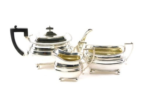 A George V silver three piece tea set, with gadrooned borders, the teapot with ebonised handle and knop, on ball feet, Sheffield 1918, 40.2oz gross.