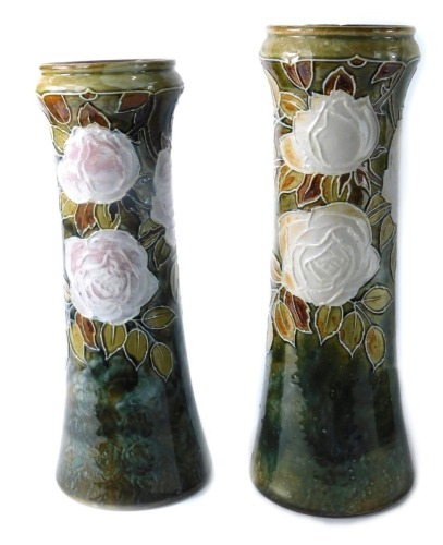 A pair of Royal Doulton stoneware vases, each with a circular top on a green glaze, with white roses, stamped to underside, 34cm high. (2, AF)