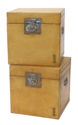 A pair of beige coloured Chinese vellum covered square boxes, each with a brass lock plate and clasp, scripted mark to bottom left, 40cm high, 40cm wide. (AF)