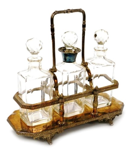 A late Victorian silver plated tantalus, with three cut glass decanters, the central decanter with a silver plated collar, each 24cm high, the stand raised on four scroll work feet, 31cm high.