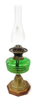 An early 20thC duplex brass oil lamp, embossed with leaves, with a green glass reservoir and clear glass chimney, raised on an octagonal wooden base, 52cm high.