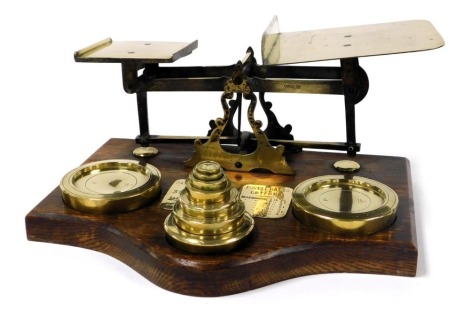 A set of early 20thC brass postage scales, raised on an oak base, with weights, from ½oz-4lbs, 38cm wide.