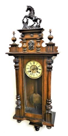 A late 19thC walnut cased Vienna wall clock, circular brass dial with chapter ring bearing Roman numerals, eight day movement with coil strike, the mask fronted pediment surmounted with a rearing horse, above a glazed front flanked by turned demi pilaster