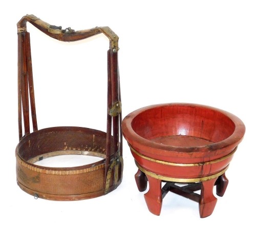 A Chinese red lacquer and brass bound rice container, raised on five spade shaped legs united by stretchers, 53cm wide, together with a bamboo and rattan circular frame with brass embellished carrying handle, 50cm wide.