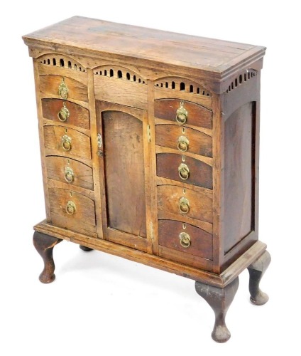 A Victorian oak apprentice chest, with a central door flanked by ten graduated drawers, raised on a base with cabriole legs, 68cm high, 58cm wide, 22cm deep.