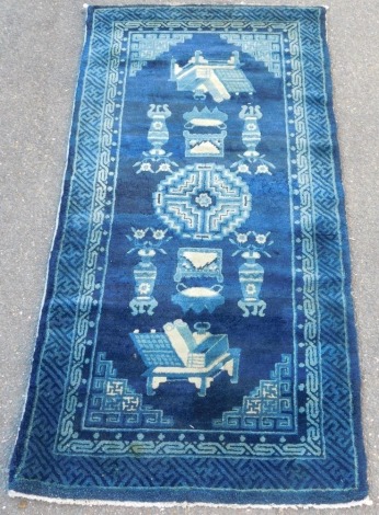 A Chinese blue ground rug, decorated with vases, furniture and Buddhist emblems, within repeating geometric borders, 150cm x 76cm.