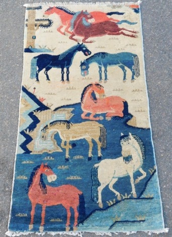 A Chinese cream and blue ground rug, decorated with eight horses, 130cm x 67cm.