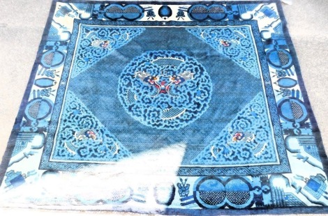 A Chinese blue ground rug, decorated centrally with dragons chasing a flaming pearl, further dragons at quarters, within a border of Buddhist emblems, 296cm x 245cm.