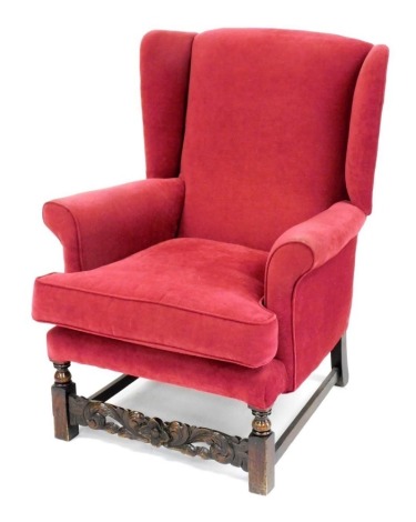 A 20thC oak framed wing back armchair, upholstered in red draylon, raised on turned and square legs united by stretchers, 75cm wide. The upholstery in this lot does not comply with the 1988 (Fire & Fire Furnishing) Regulations, unless sold to a known expo