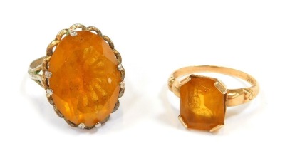 Two dress rings, comprising a rectangular cut citrine, in a raised basket, on yellow metal band stamped 14K, size O, 6g all in, and a silver and imitation citrine dress ring. (2)