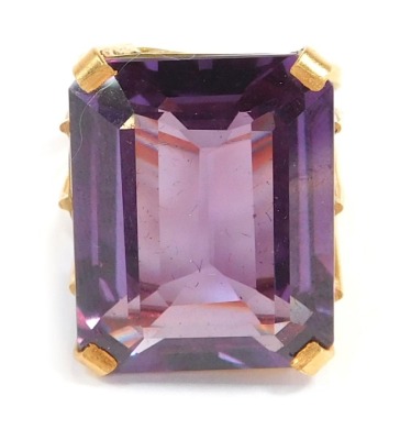 An imitation amethyst dress ring, the rectangular cut stone in a raised basket, with four claw setting, on a four rowed yellow metal band, unmarked, ring size O, 14g all in.