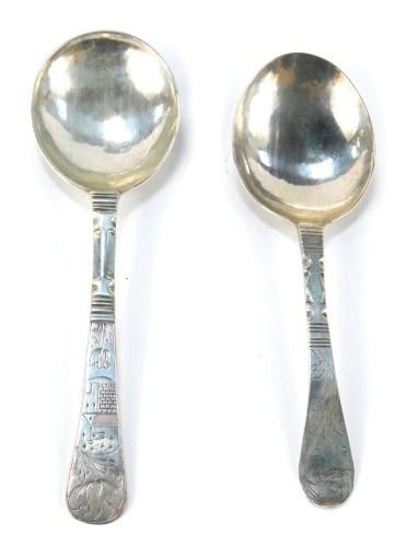 Two white metal caddy spoons, each with a circular bowl initialled verso, both handles bright cut decorated with foliate motifs, one with a depiction of a building, 0.7oz.