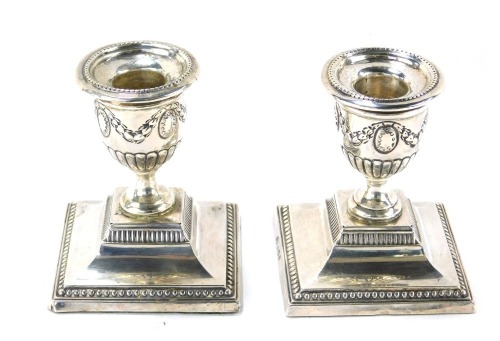 A pair of Edward VII silver dwarf candlesticks, each with Neoclassical swag decoration, on square foot with weighted bases, maker CB, Birmingham 1906, 8cm high.