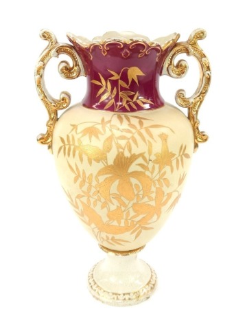 A 19thC pottery two handled vase, of baluster form, decorated with gilt heightened flowers and leaves, against a cream and cranberry ground, on a socle base, unmarked, 43cm high.