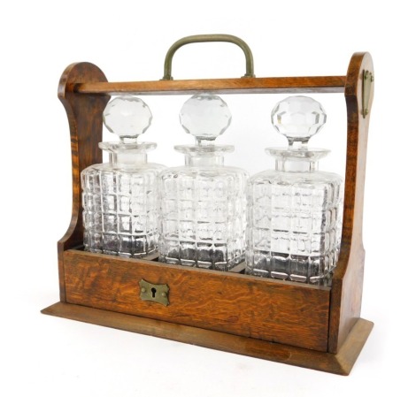 A 20thC oak cased Tantalus, containing three moulded glass square faceted spirit decanters, the Tantalus 31cm high.