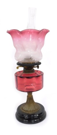 A Victorian cranberry glass oil lamp, the flared shade with etched floral detail and a cranberry glass reservoir, on brass stemmed base with ebonised knop ends, 48cm high overall. (AF)