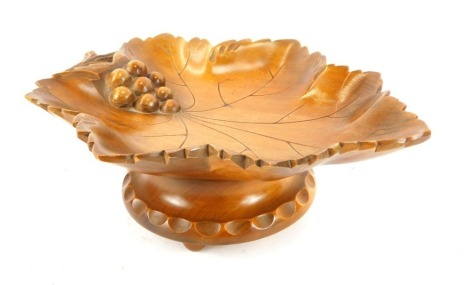 A Black Forest pine musical dish, carved as a vine leaf with grapes, on a circular base, with musical movement, raised on three ball feet, 22cm wide.