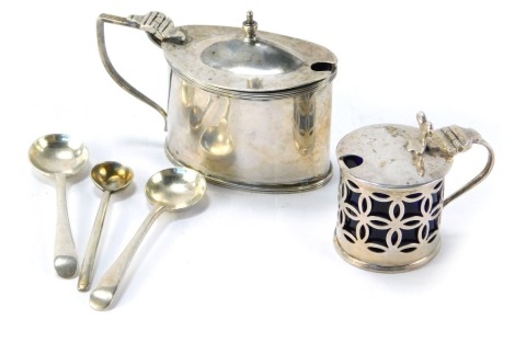 Two silver mustard pots, comprising an oval shape mustard with blue glass liner, George V, and a smaller pierced cup example, with rubbed marks, and two silver serving spoons, 3oz gross, and additional silver plated preserve spoon. (5)