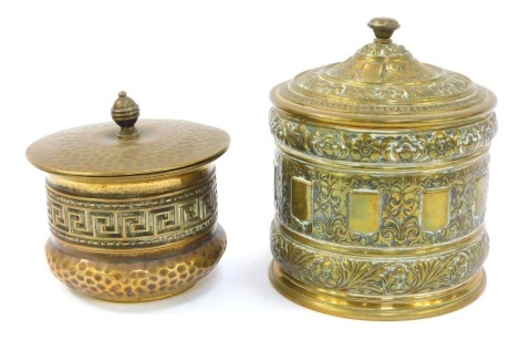 Two late 19thC/early 20thC brass tobacco jars, both of cylindrical form, one impressed with floral motifs, leaves, etc, 15cm high, the other with a band of Greek key decoration, 10cm high. (2)