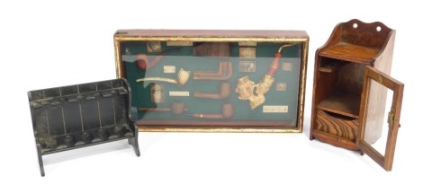 A group of smoking related items, to include a display case containing various reproduction pipes, 52cm wide, painted pipe stand and an oak smoker's stand, lacking bowl, 31cm high. (a quantity)