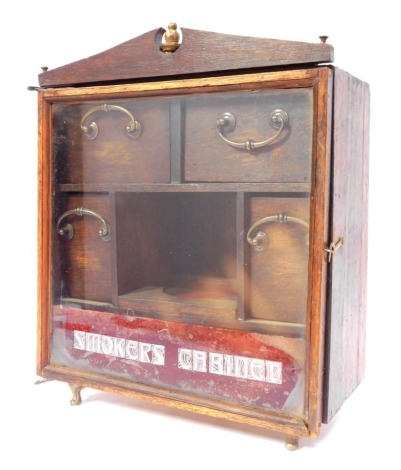 A 20thC oak smoker's cabinet, the glazed door enclosing an arrangement of drawers, signed written Smokers Cabinet, 25cm high.