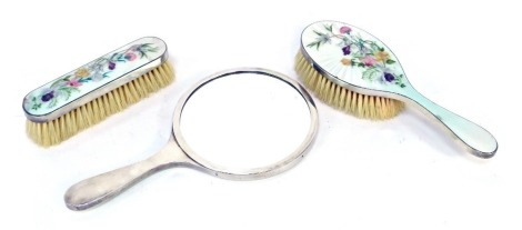 A Queen Elizabeth II silver and pale green guilloche enamel three piece dressing table set, overpainted with flowers, comprising hand mirror, clothes and hairbrushes, London 1956.