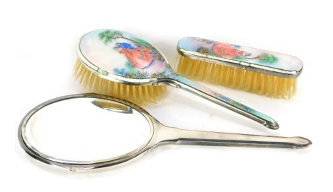 A George VI silver and white guilloche enamel three piece dressing table set, painted with a gallant and lady, in a garden setting, comprising hand mirror, hair and clothes brushes, Birmingham 1947.