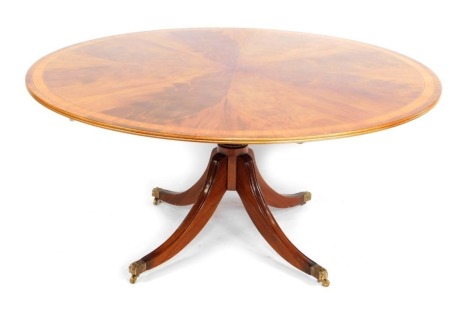 A reproduction flame mahogany inlaid dining table, the circular top raised on a turned column, on sabre legs, with brass lion paw capped castors, the top 72cm high, 153cm diameter.