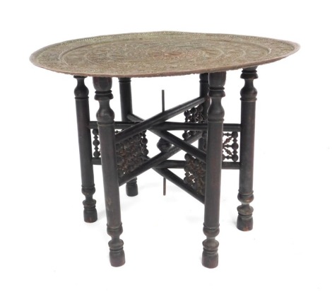 An early 20thC Indian copper tray topped table, with pierced and embossed decoration of repeating fish, birds, leaves and animals, raised on an ebonised folding base, 45cm high, 61.5cm wide.